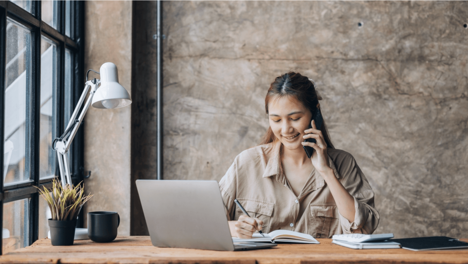Student calling university admissions on phone, looking at laptop screen with inquiry